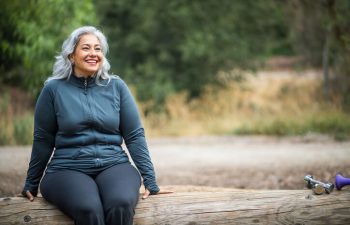 Smiling overweight mature woman sitting on a tree log.