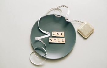 A plate with a measuring tape and scrabble pieces that read eat well.