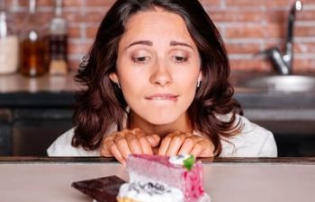 A woman trying to overcome her craving for sweets looking at a plate with cakes.