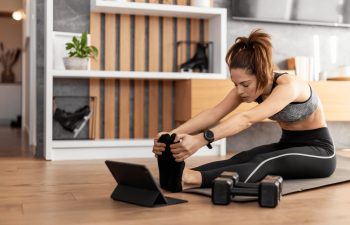 A young fit woman doing stretching exercises in front of her laptop on a floor at home.