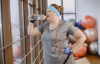 An obese woman with a jumping rope drinking water after set of exercises she did at the gym.
