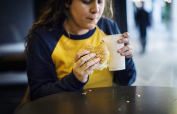 Overweight teenage girl eating a burger and having a fizzy drink.