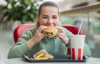 Overweight young woman eating burger and fries at fast-food restaurant.