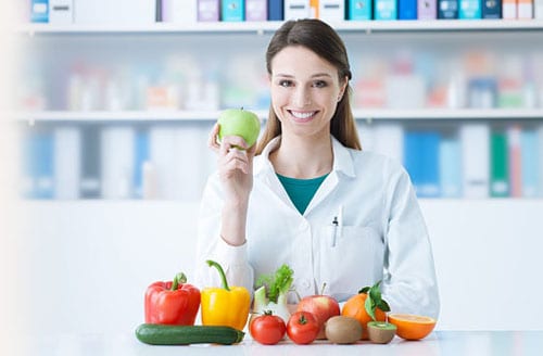 A female doctor at a table with fruit and vegetables.