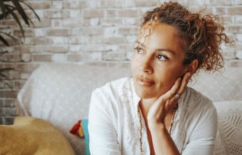 pensive woman in tight curly hair sitting on the couch