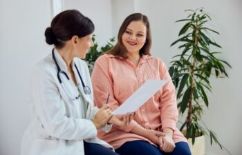 A satisfied female nutritionist holding a paper with weight loss progress and smiling with an overweight female patient.